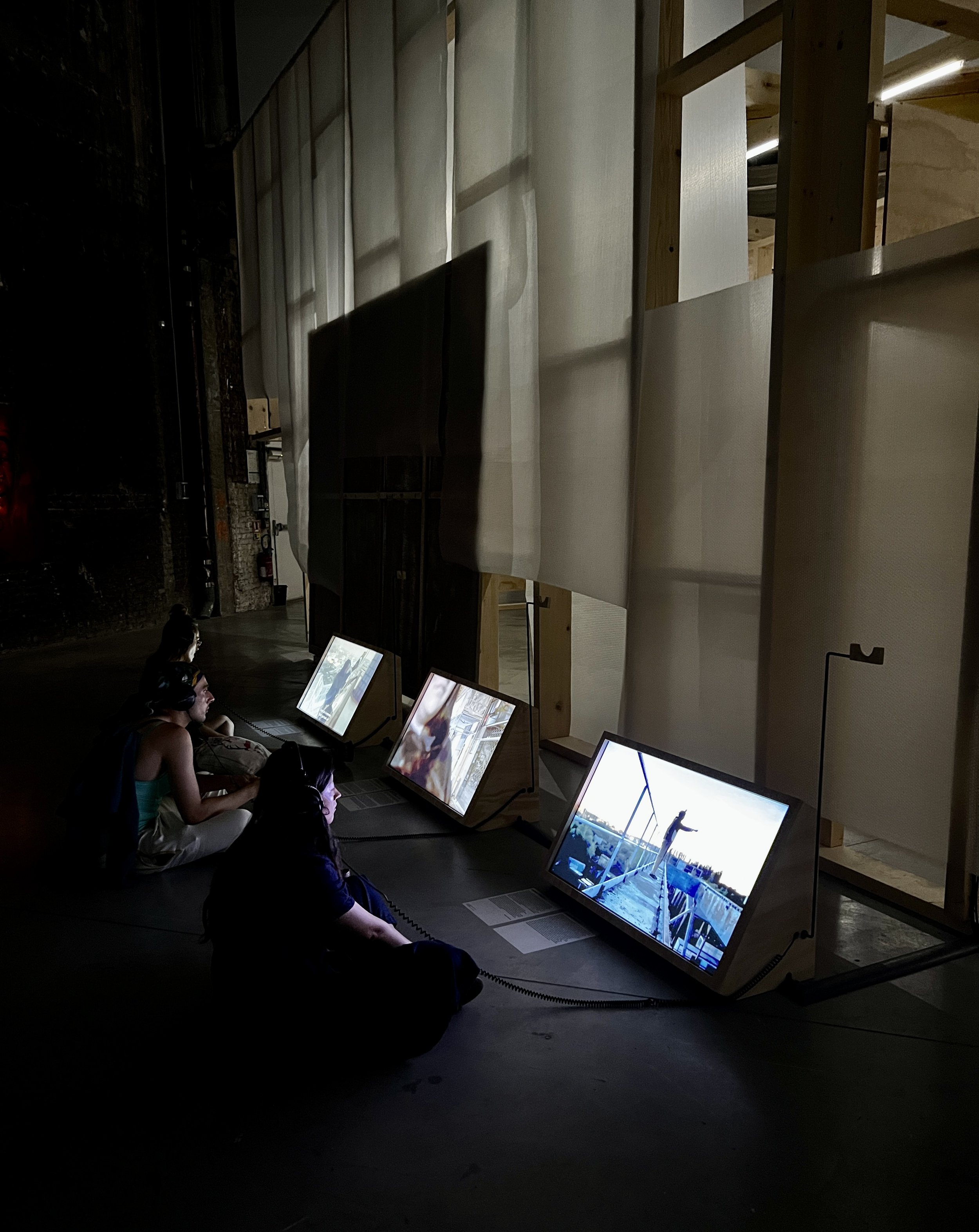 People sitting on the floor in front of illuminated screens displaying digital artwork in a dark room.