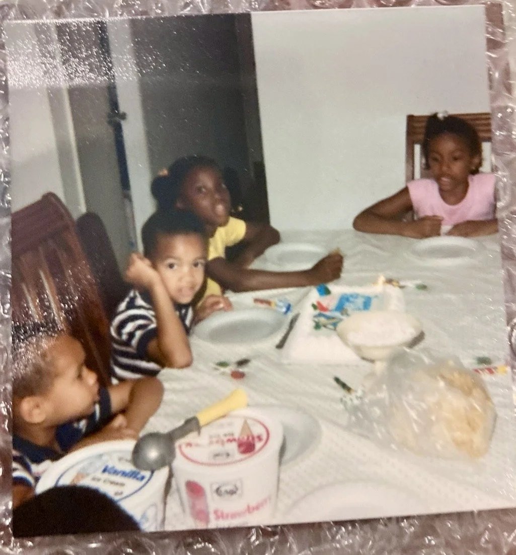 Childhood ETHAN WARD sitting at a dining table with friends and family with plates, yogurt, and snacks, celebrating around a cake with pink frosting.