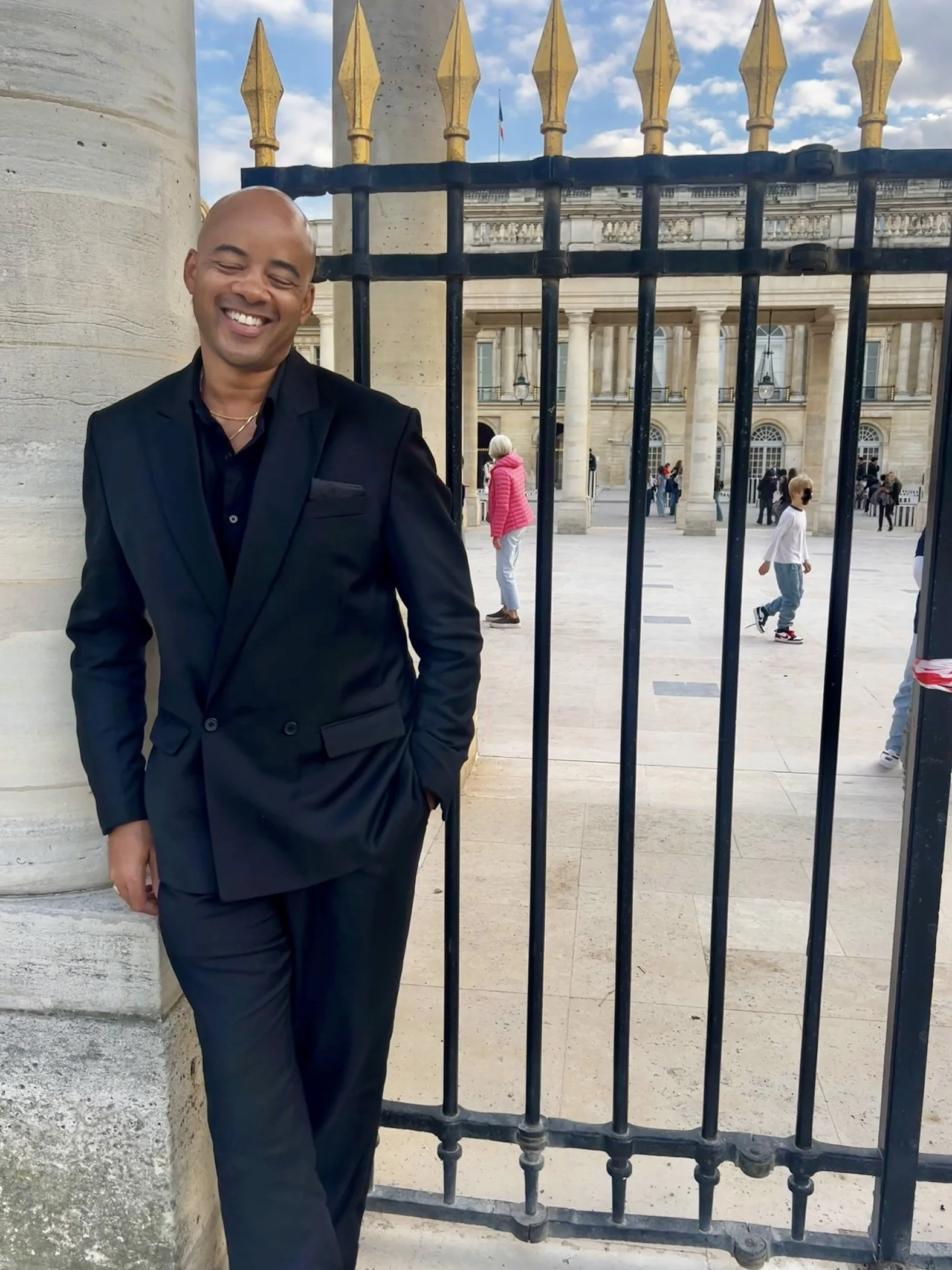 Ethan Ward stands in Paris smiling and wearing a black suit.