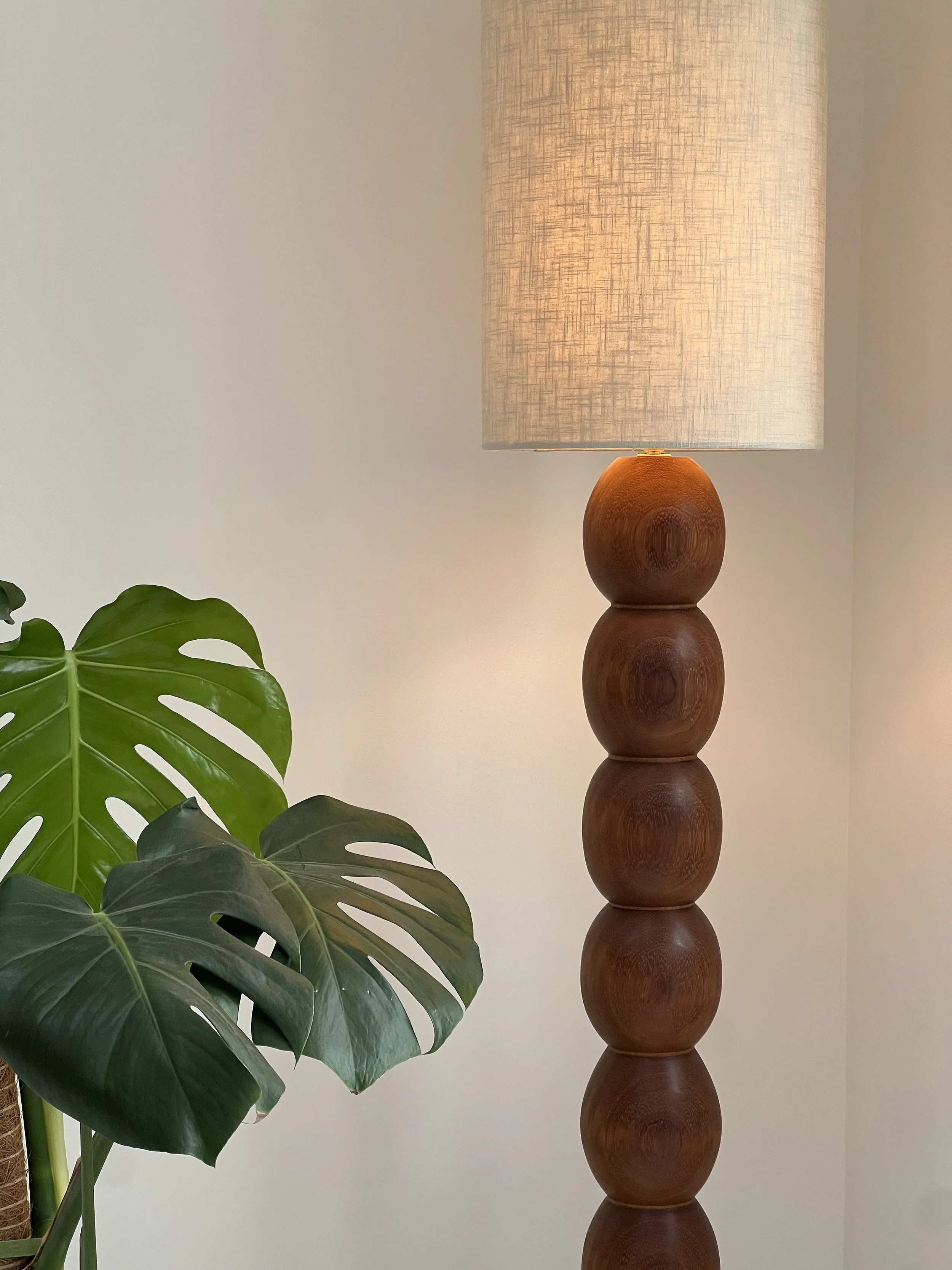 Tall sculptural wooden floor lamp with stacked spherical base and beige fabric drum shade in a minimalist modern interior.
