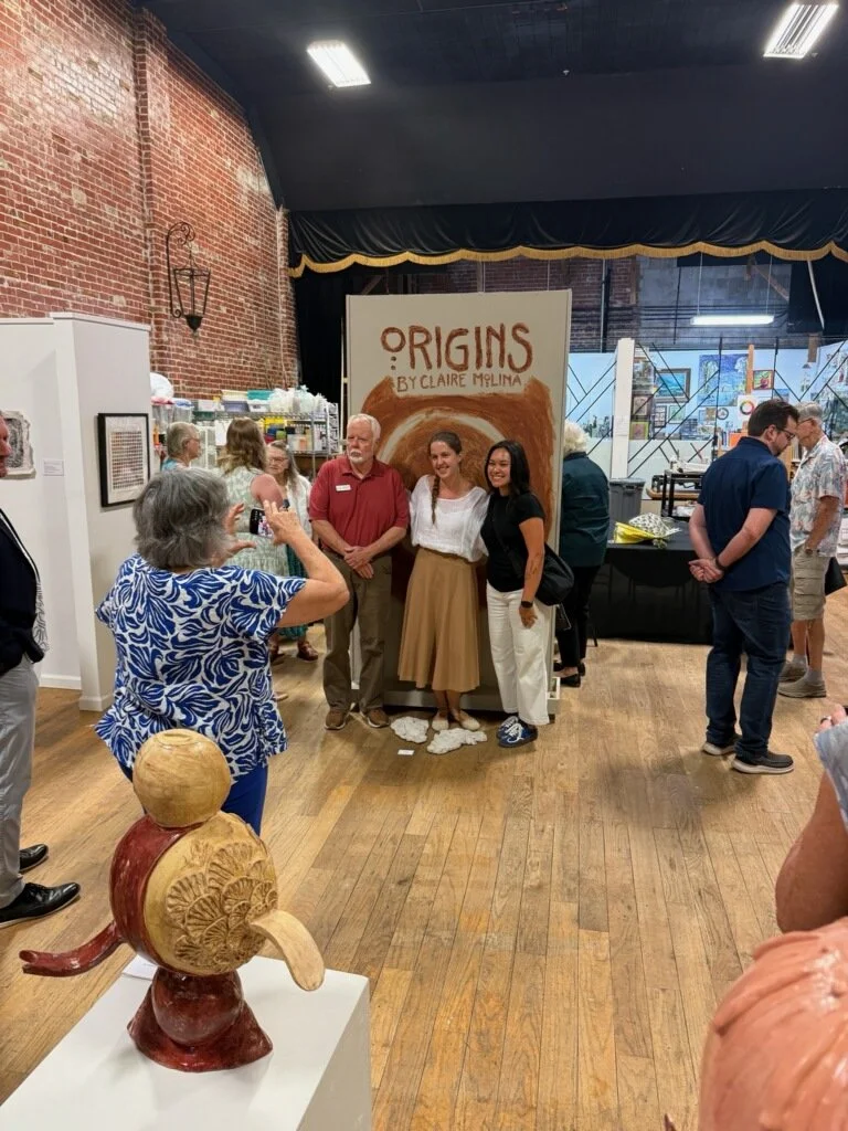 interior view of the gallery during the opening reception showing three individuals getting photographed in front of the gallery moving wall