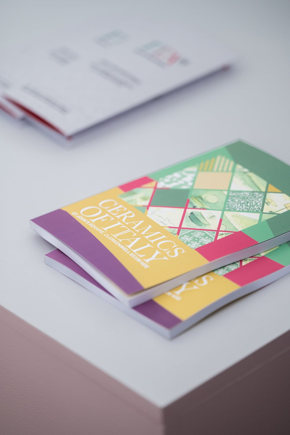 Brochures on generative artworks with colorful geometric designs, placed on a white table with a blurred document in the background.