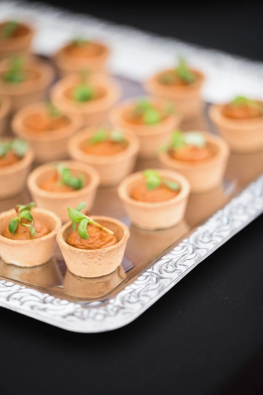 Mini appetizer cups with a red sauce and topped with green herbs on a silver tray.