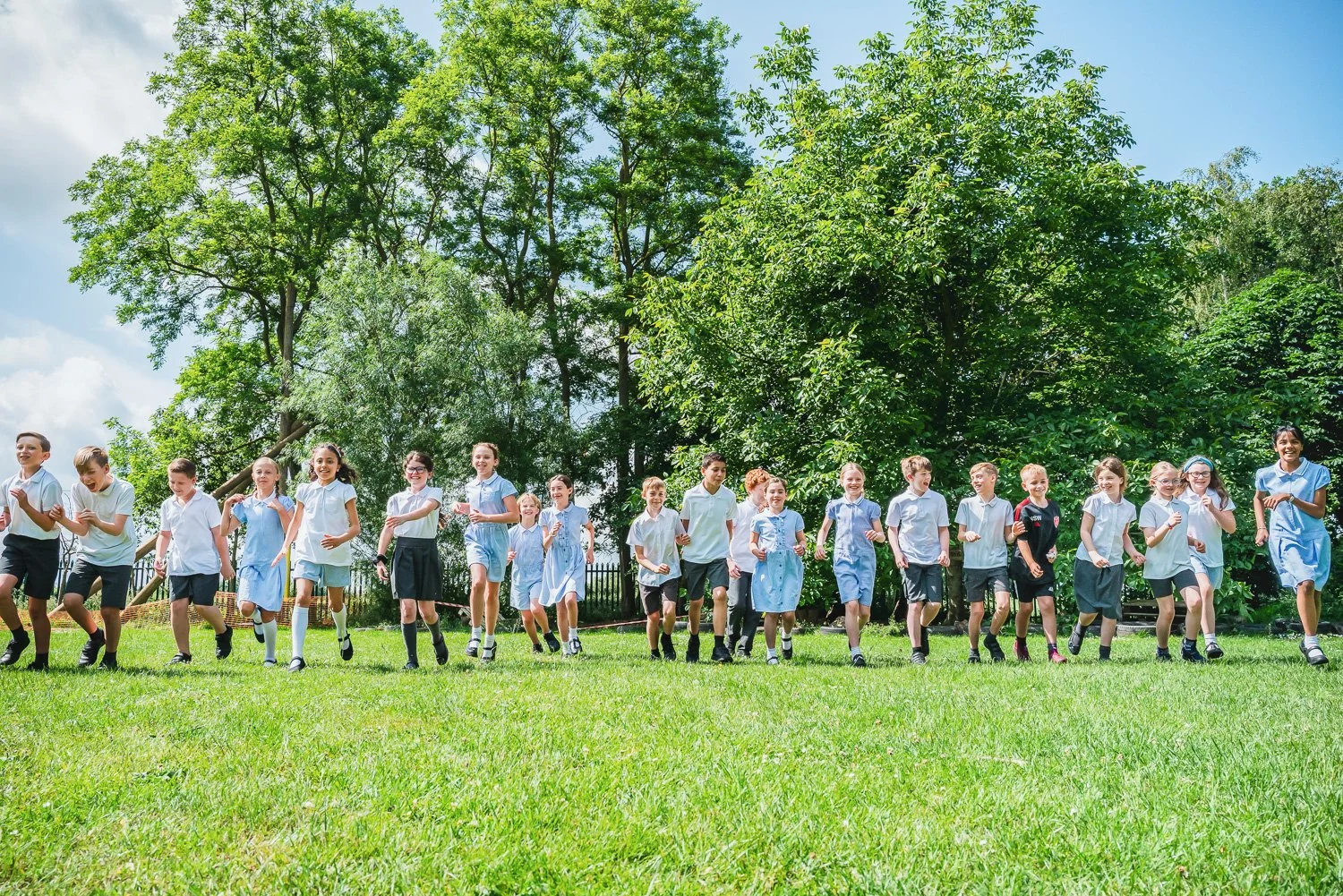 Group of children running on a grassy field outdoors with trees in the background.