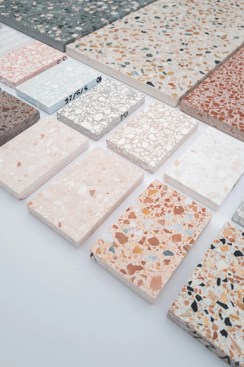 Sample rectangular terrazzo tiles in various colors and patterns laid out on a white surface for display.