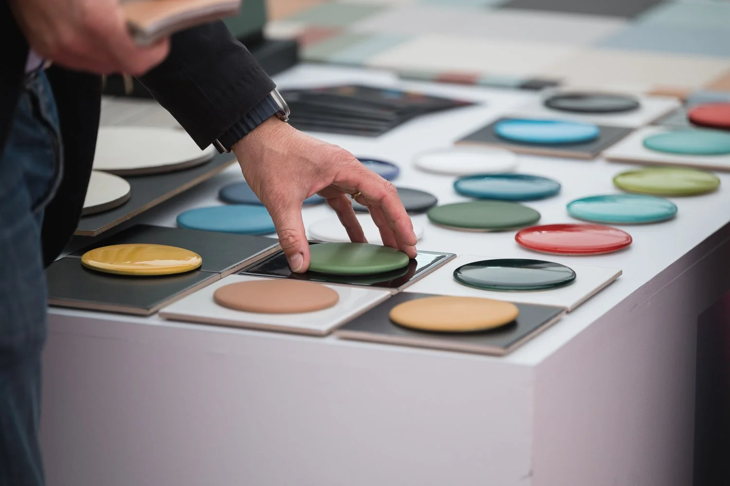 A person is selecting a green color sample from a display of various color samples arranged on a table.