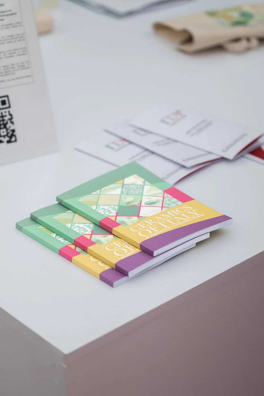 Colorful flyers or brochures labeled "Ceramics of Italy" on a white table, with some papers and a carton visible in the background.