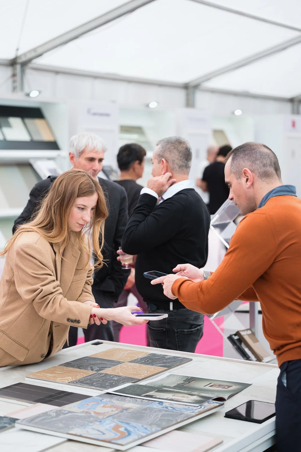 People at an exhibition booth examining samples and using smartphones.