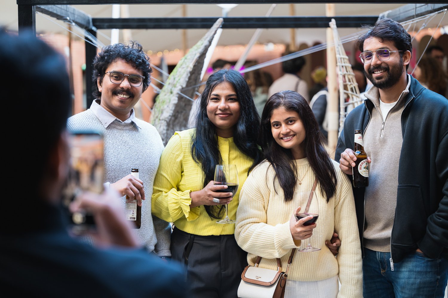 Four friends at a social gathering, holding drinks, smiling for a group photo