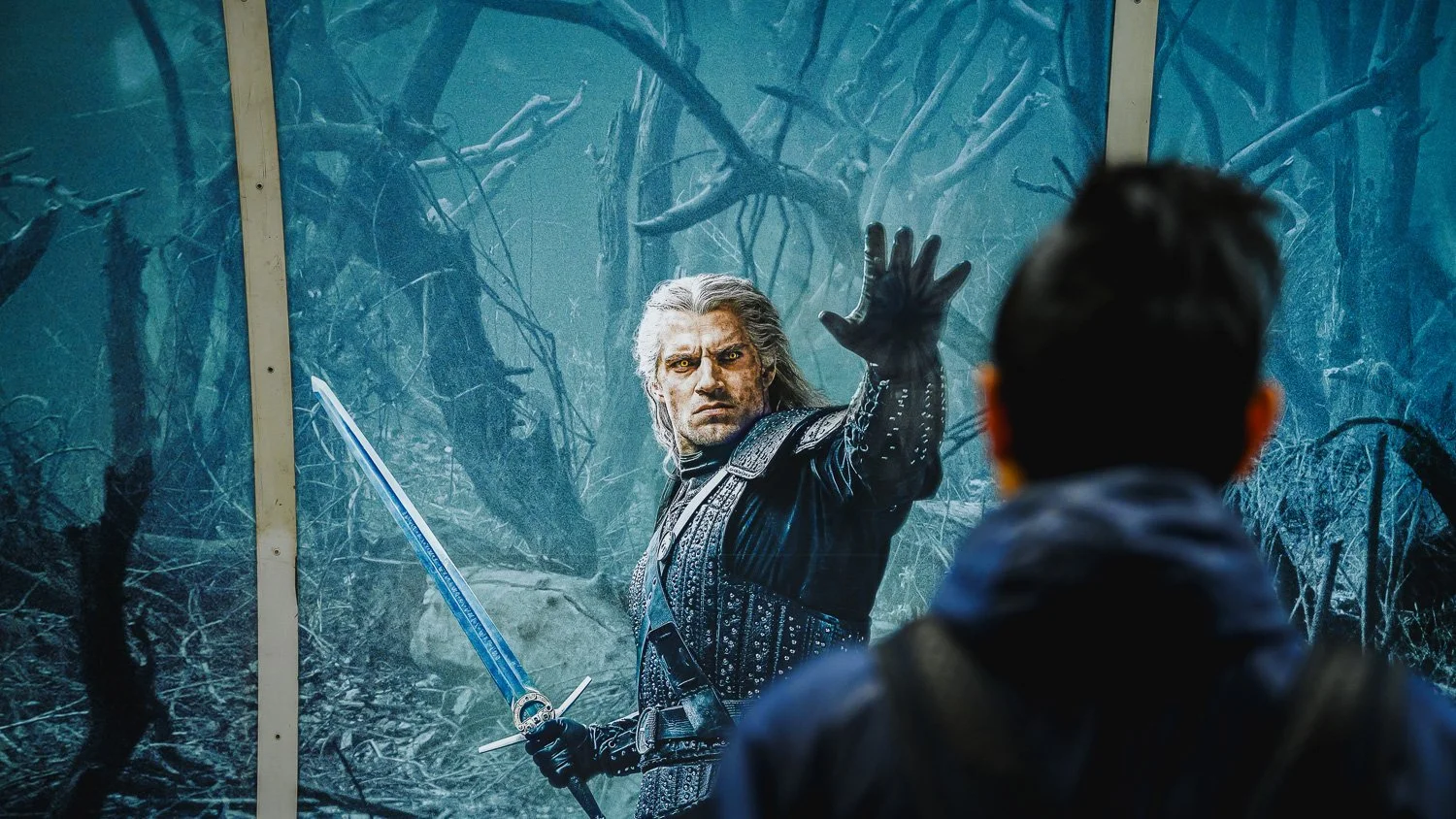A man dressed as a fantasy character with a sword in a blue forest scene, gesturing with his hand to a person in the foreground. Phocus Collective O-O-H Photography.