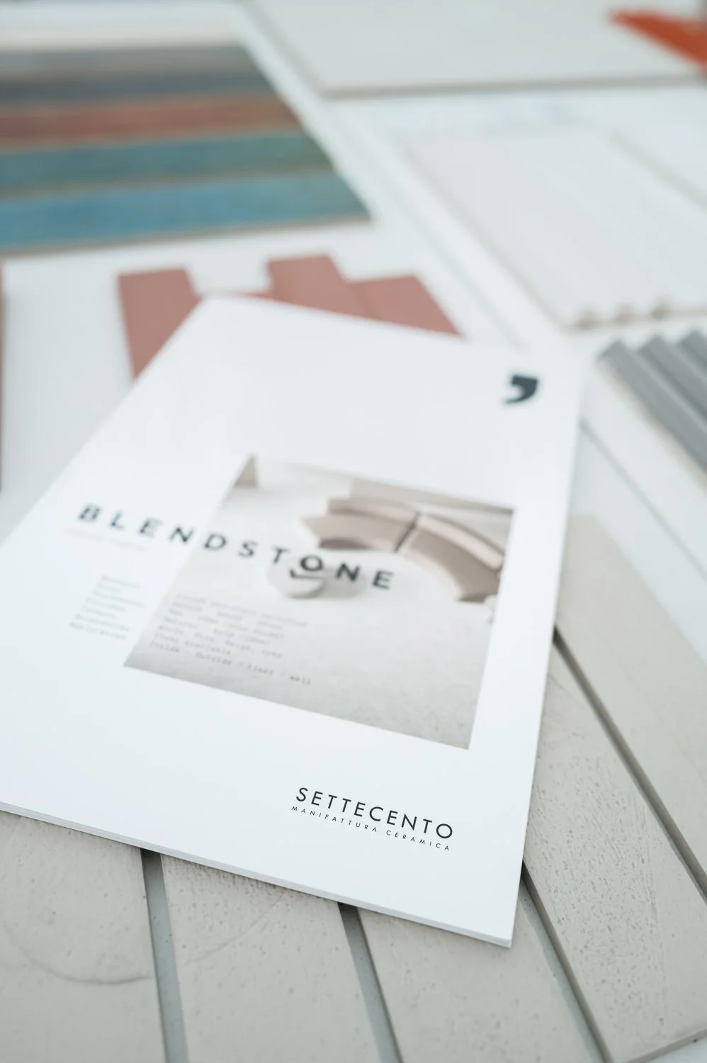 Ceramic tile samples and a brochure for Settecento, a ceramic manufacturing company, on a tiled surface.