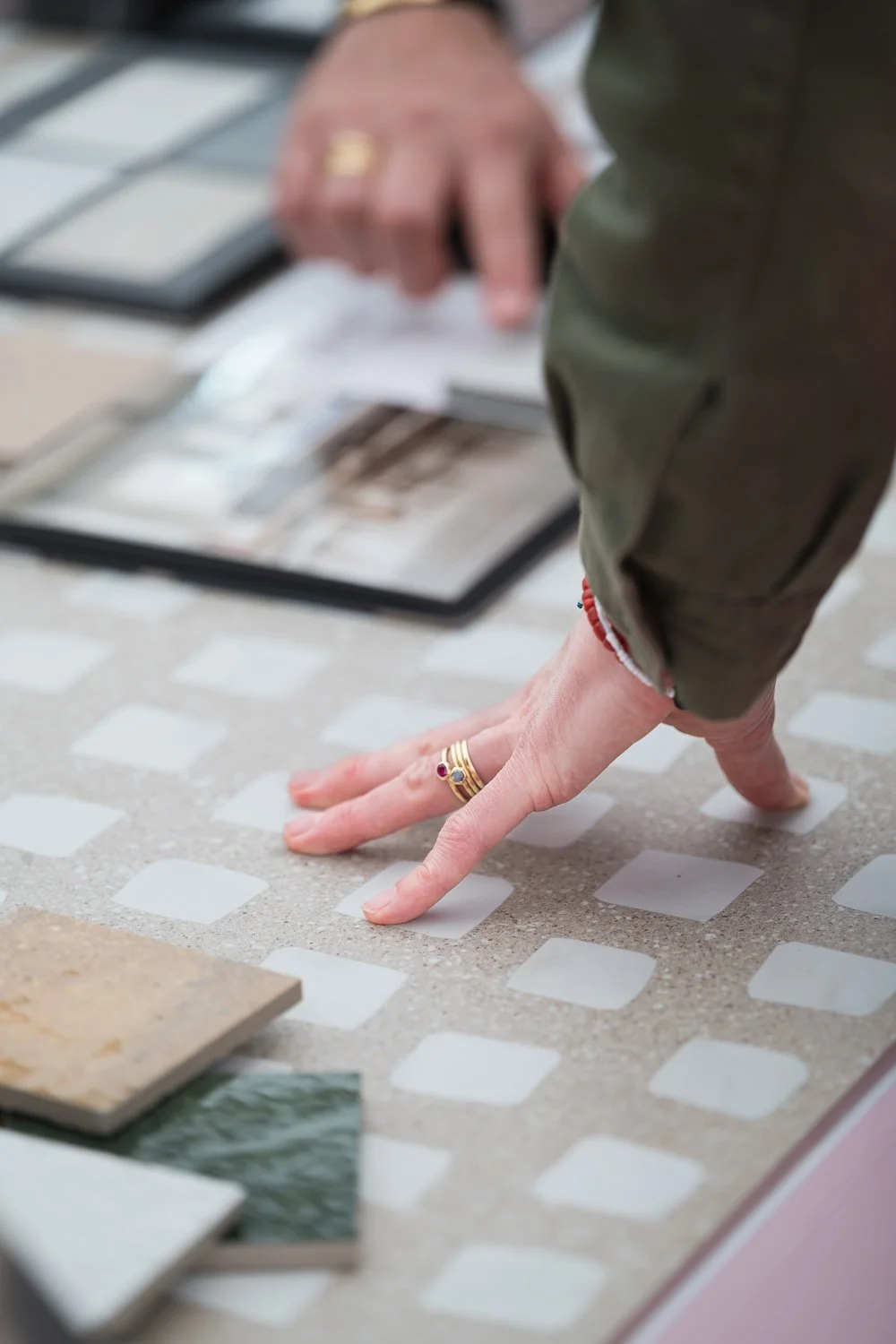 Person testing floor tiles by hand, wearing multiple rings, with sample tiles and photographs on display.