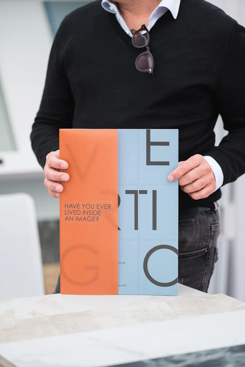 Person holding a brochure with the question 'Have you ever lived inside an image?' on the front cover, featuring a design split into orange and blue sections.