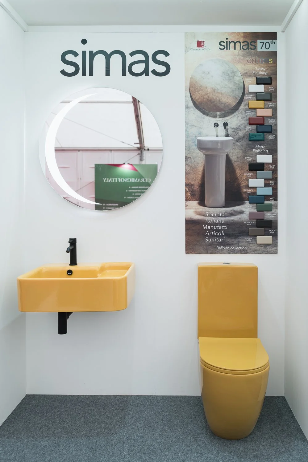 A yellow bathroom sink and toilet with a large mirror and a color display poster on the wall showcasing different finishes and colors for bathroom fixtures.