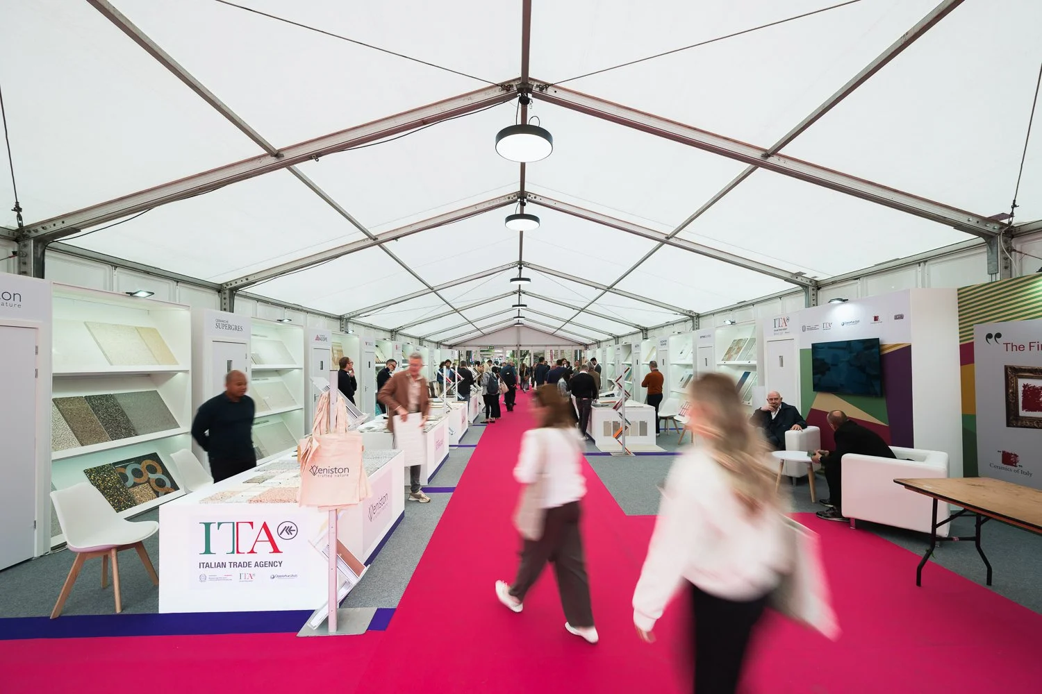 An exhibition tent with booths and displays, featuring the Italian Trade Agency, with people walking and interacting.