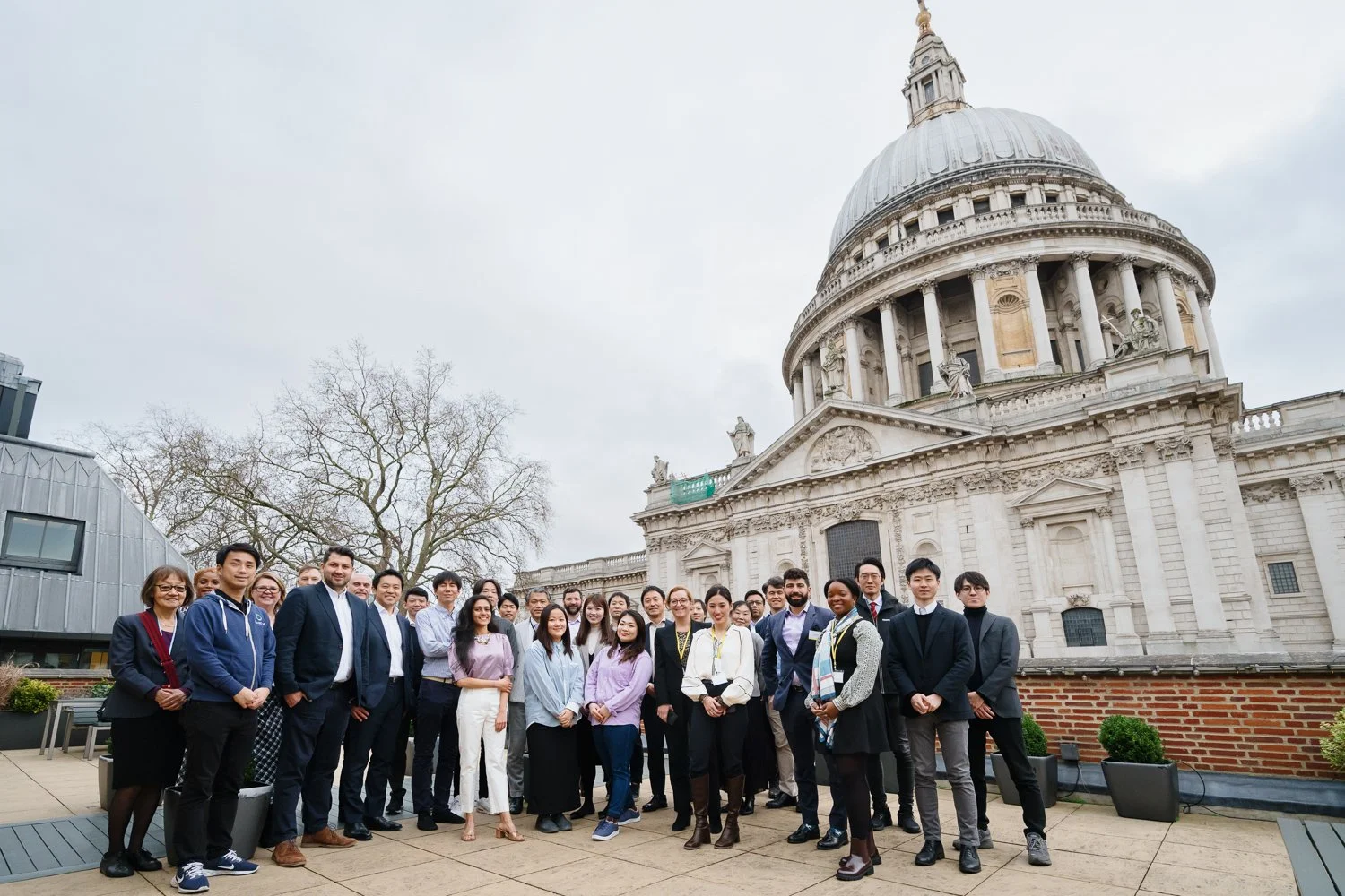 A diverse group of people gathered outside St. Paul's Cathedral in London, England, with the historic building and overcast sky in the background.