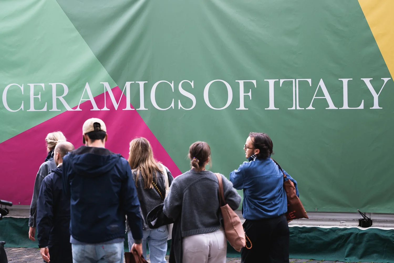 Group of people standing in front of a large colored banner that reads 'CERAMICS OF ITALY'.