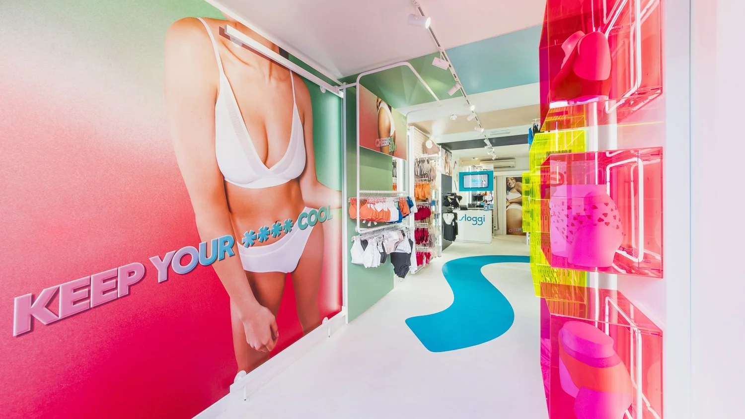 Colorful retail store with large advertisement of a woman in white lingerie on the left wall, clothing and accessories on display, and bright neon pink and green shelves on the right, with a blue curving path on the floor.