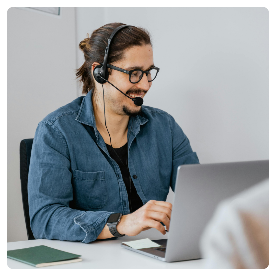 Man with glasses and a headset working on a laptop in an office.