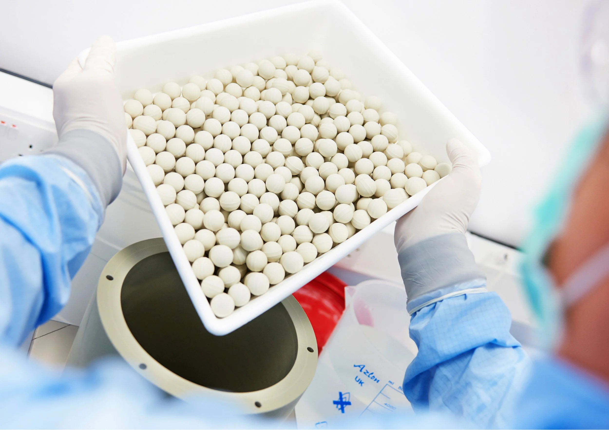 Medical worker in gloves and gown holding a tray of small white pills.