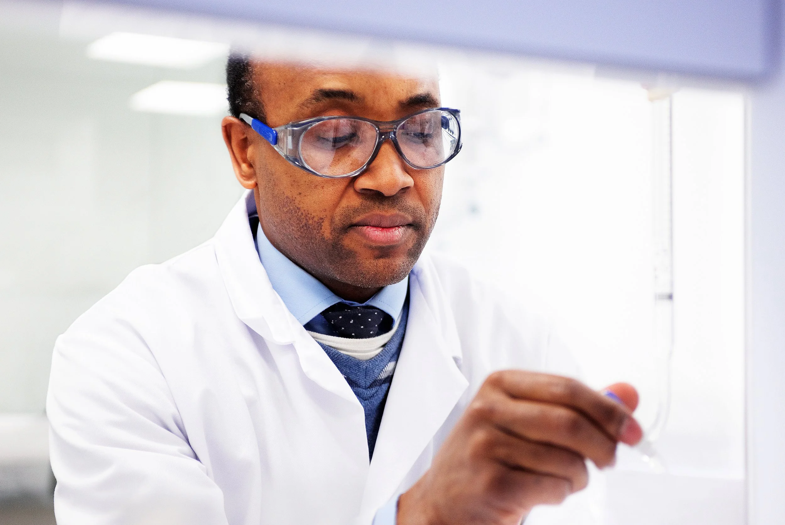 A scientist wearing safety glasses and a white lab coat working in a laboratory.