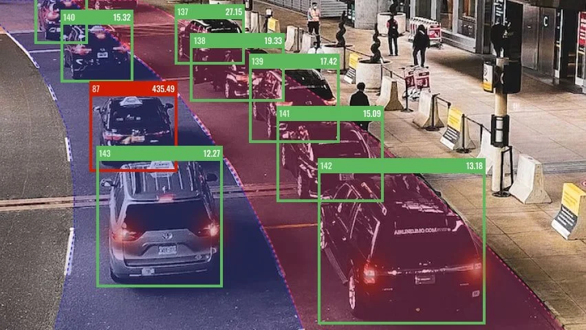 Image showing a parking lot with several cars, some identified by bounding boxes with confidence scores. A sidewalk and people walking are visible on the right side.