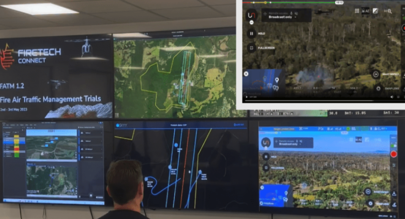 Multiple screens displaying fire management data, maps, and drone footage, with a person observing in front of them.