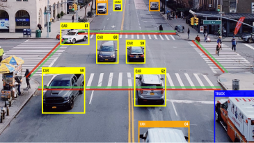 A busy city street with crosswalks and multiple vehicles including cars and trucks, some labeled with yellow and blue bounding boxes, indicating they are cars or trucks.