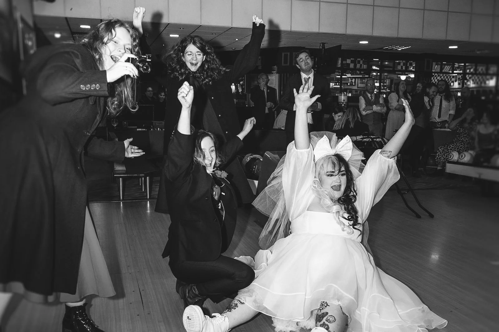 Group of women celebrating and taking photos at a party, with one woman in a wedding dress dancing on the floor.