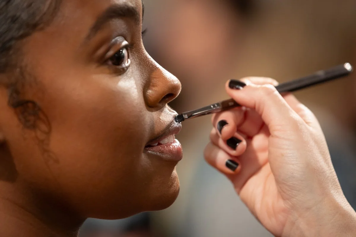Close-up of a makeup artist applying lip makeup during a beauty demonstration.