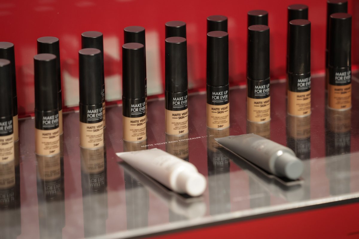 Row of Make Up For Ever foundation products arranged on a display counter at a beauty trade show.