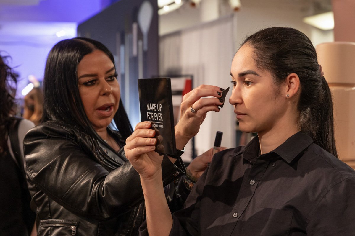 Makeup artist applies eye makeup to a model during a live beauty demonstration at The Makeup Show.