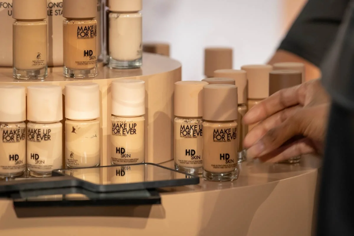 Rows of cosmetics and foundation products arranged on a display shelf at The Makeup Show.