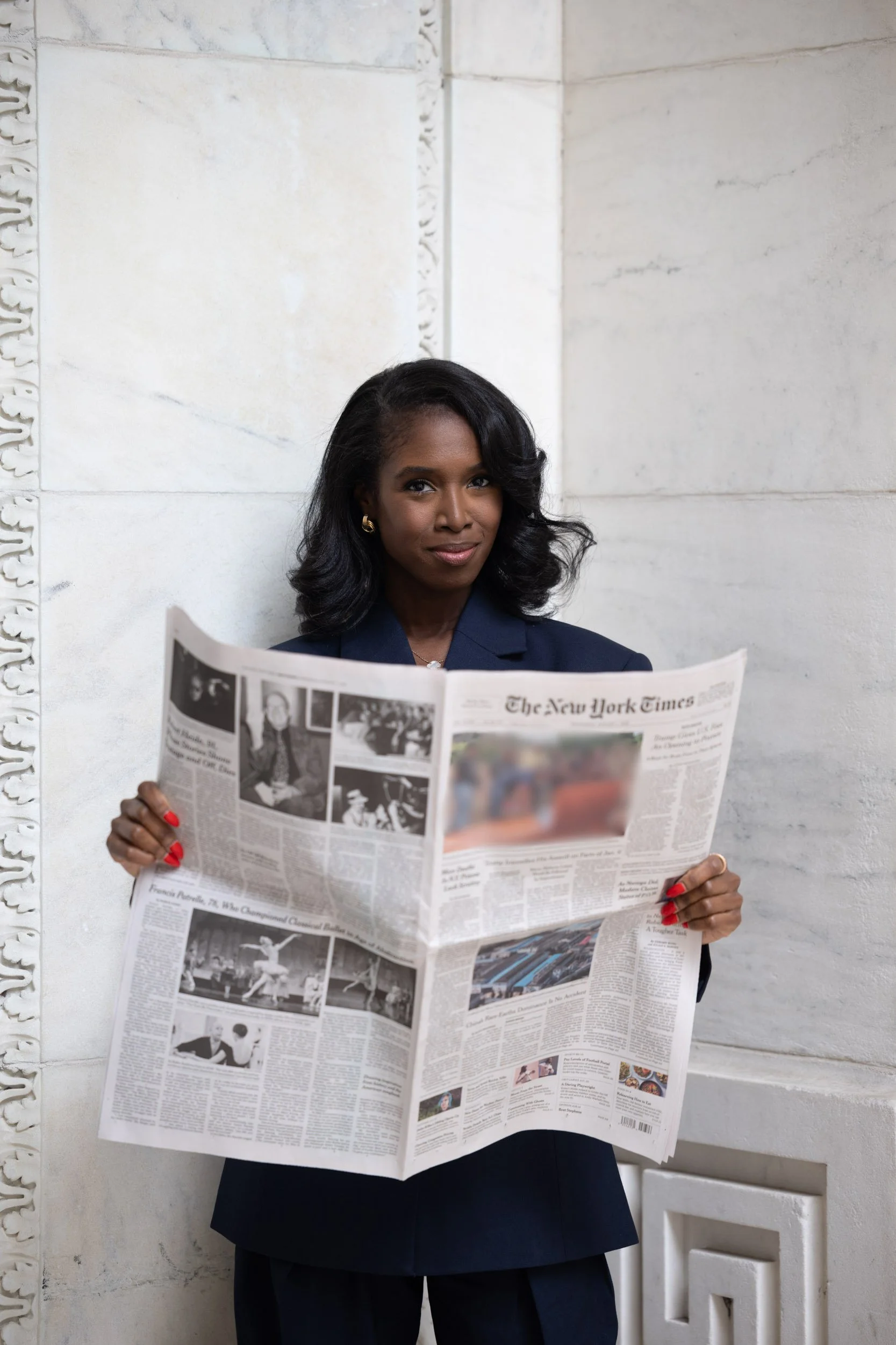 Copywriter for luxury brands holding a copy of the New York Times and smirking at the camera