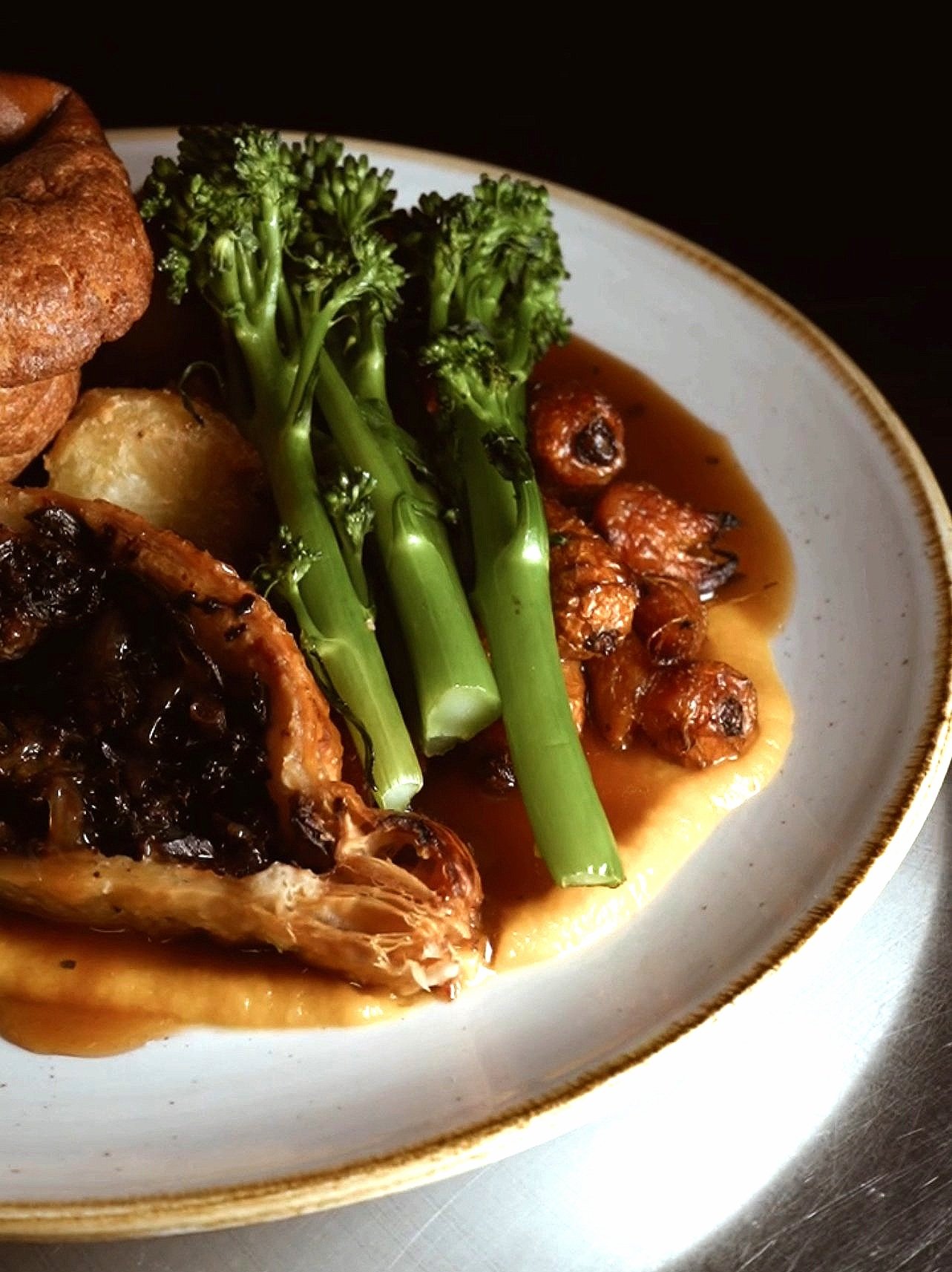 Plate with broccoli, roast vegetables, mashed potatoes, and a meat dish with gravy.
