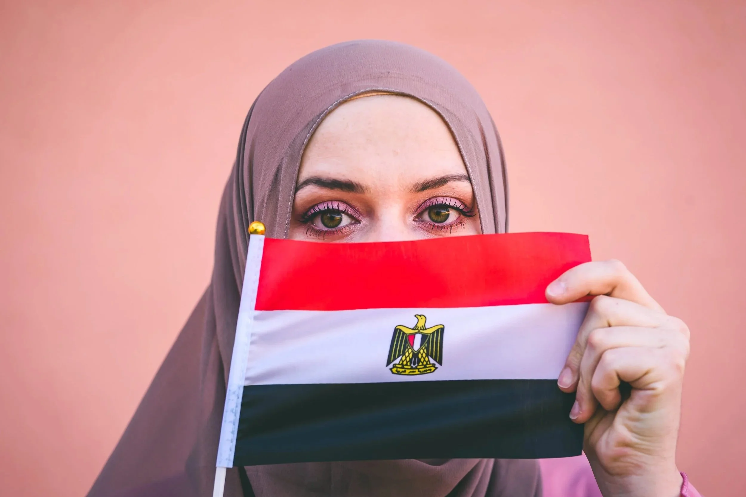 Egyptian woman - eyes visible - holding an Egyptian flag across her face