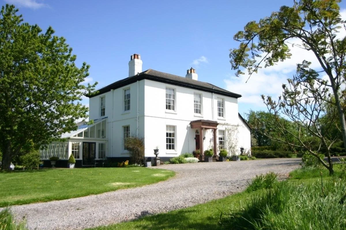 Large white painted country property surrounded by trees. gravel drive leading to front door
