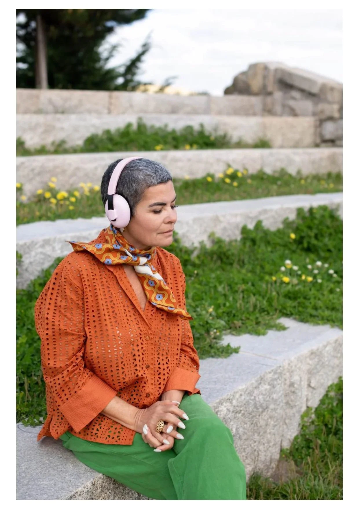woman seated quietly att the park listenign to headphones, looking calm