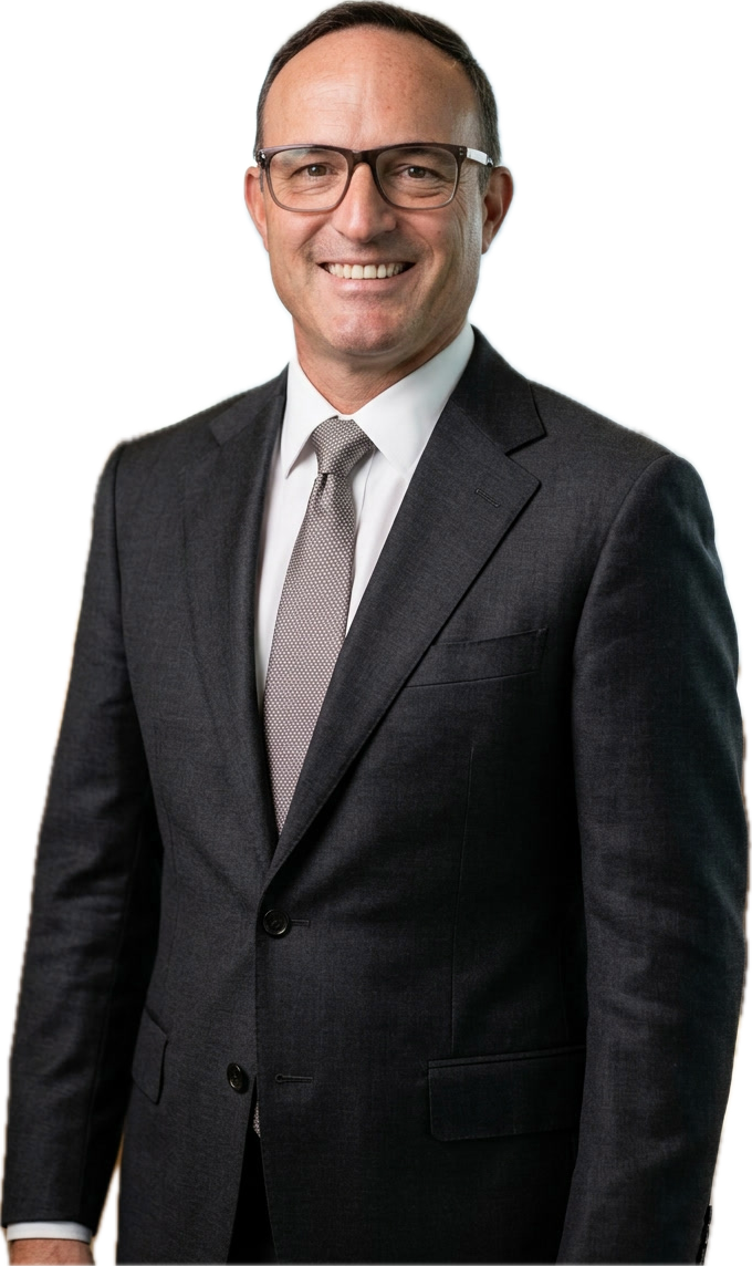 A man wearing glasses, a dark suit, white shirt, and a white tie, smiling and standing against a white background.