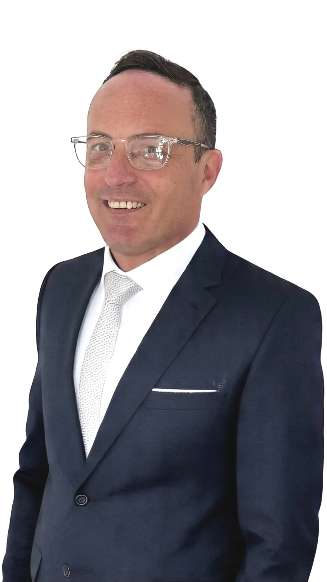 A man wearing glasses, a dark suit, white shirt, and a white tie, smiling and standing against a white background.