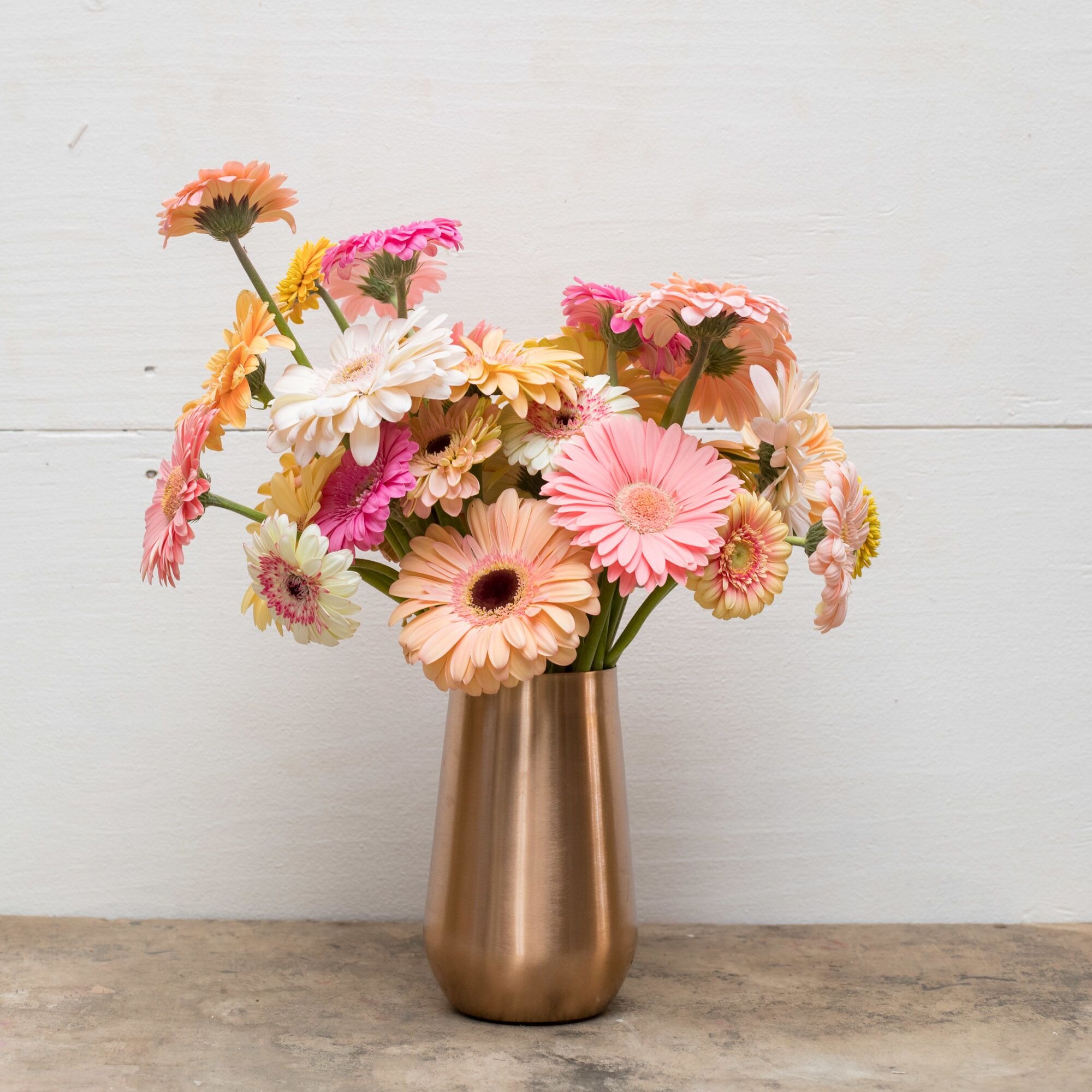 A bouquet of pink, peach, yellow, and ivory daisies in a rose gold colored vase