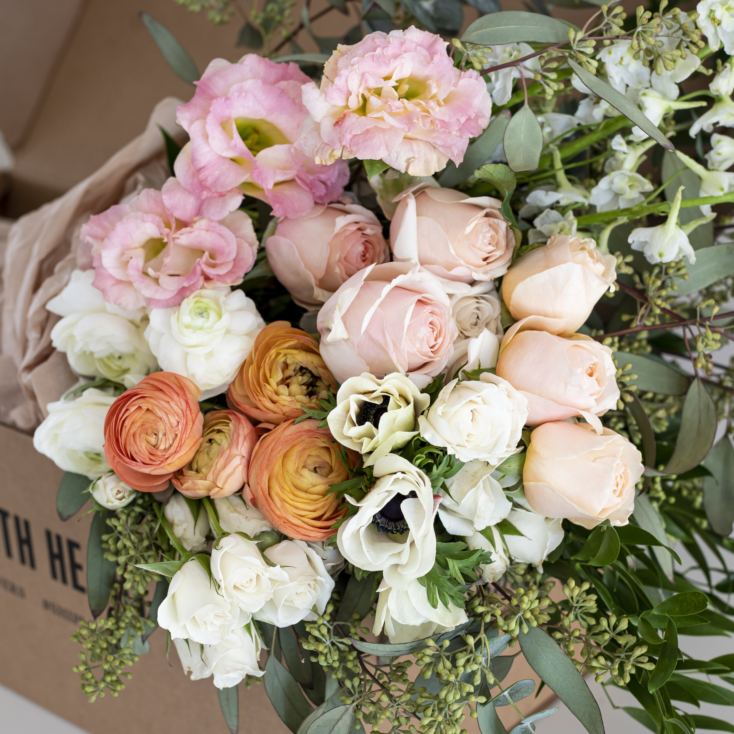 A bouquet of mixed white, pink, and orange flowers wrapped in burlap, sitting in a cardboard box