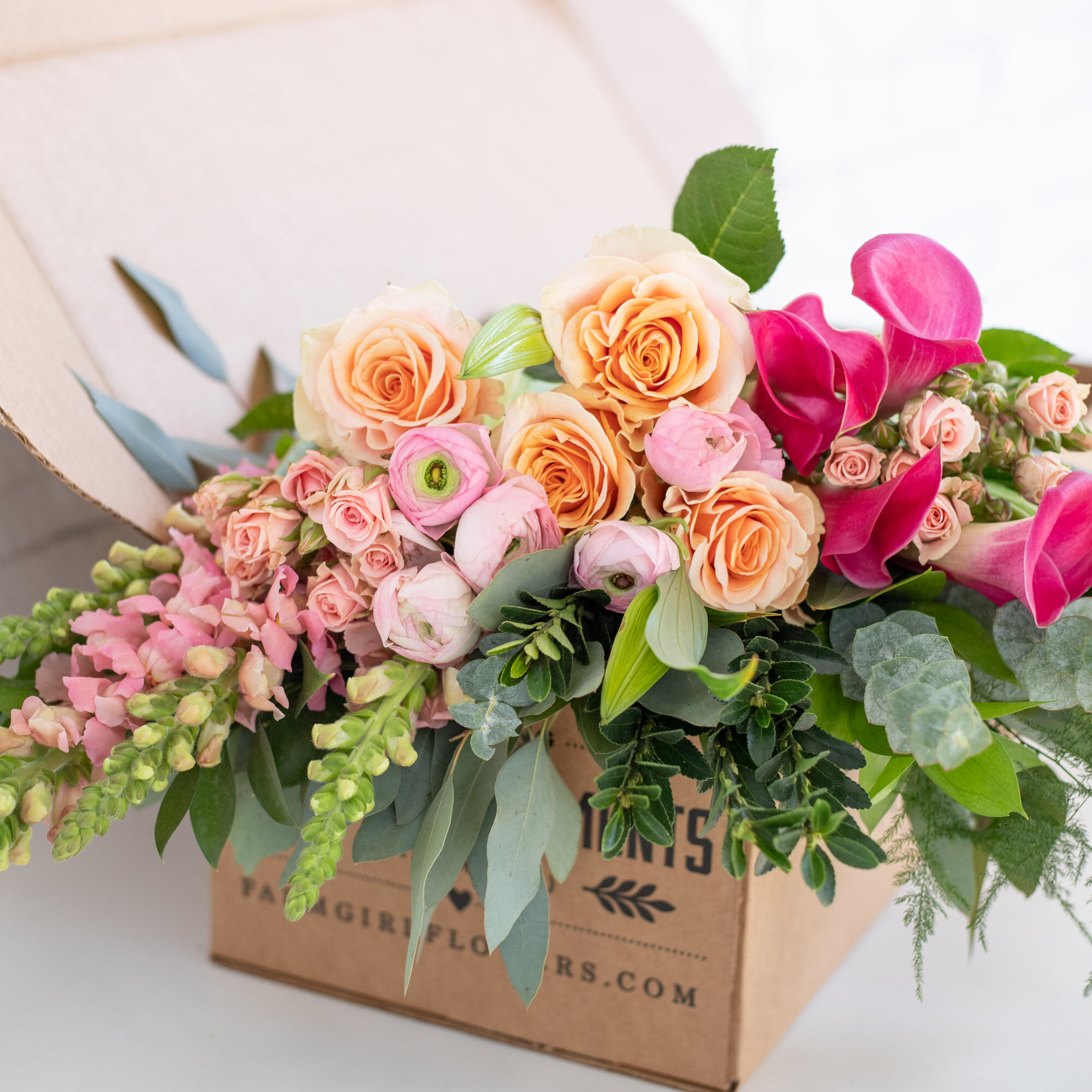 A bouquet of mixed white, pink, and peach flowers wrapped in burlap, sitting in a cardboard box