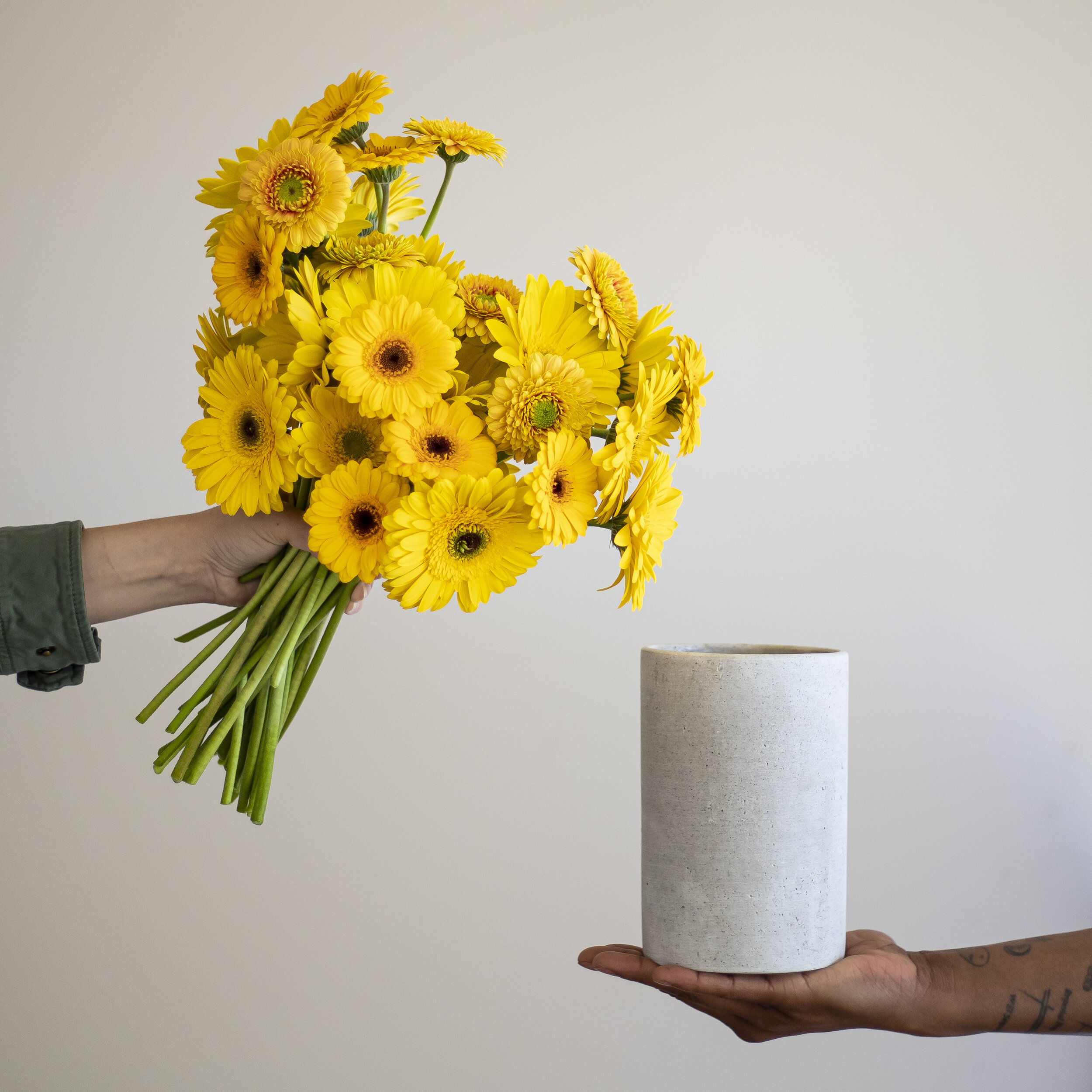 A bouquet of yellow daisies being held in one hand, with a white stone vase held in another hand