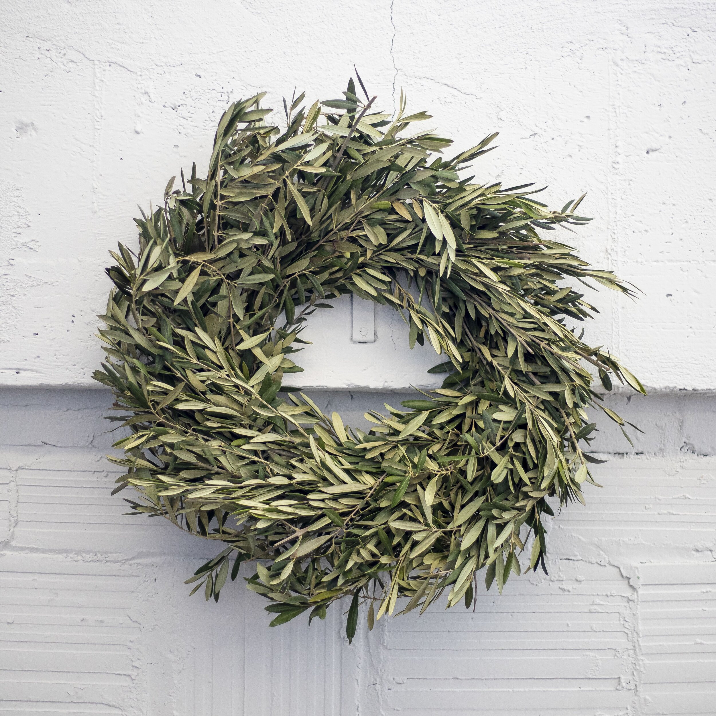 A dried green wreath hanging on a white concrete wall