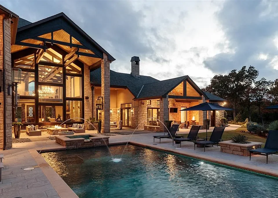 A luxurious backyard with a swimming pool, outdoor lounge chairs, an umbrella, and a large house with modern architecture and extensive glass windows.