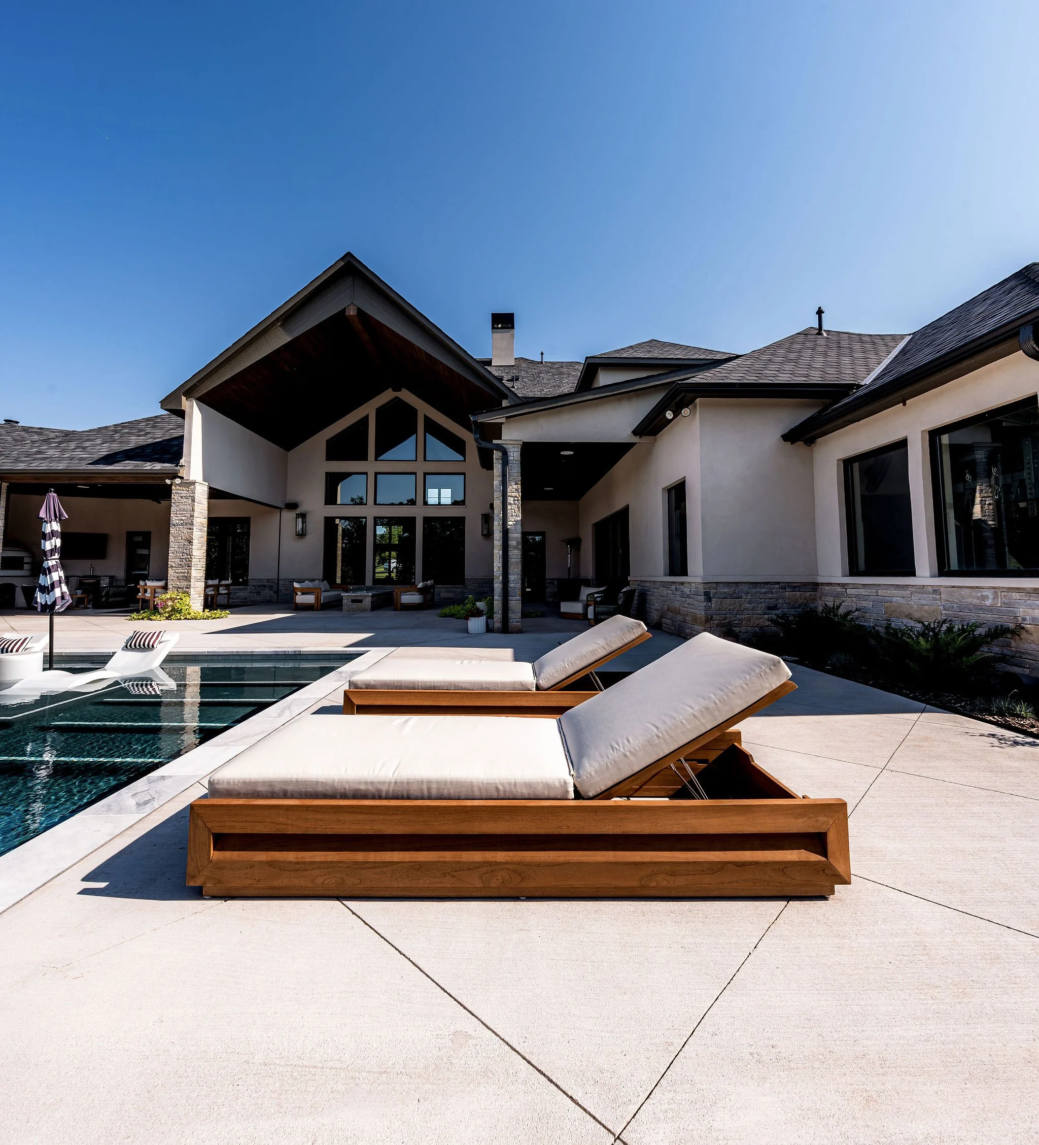 Backyard with a swimming pool and two white lounge chairs, modern house with large windows in the background