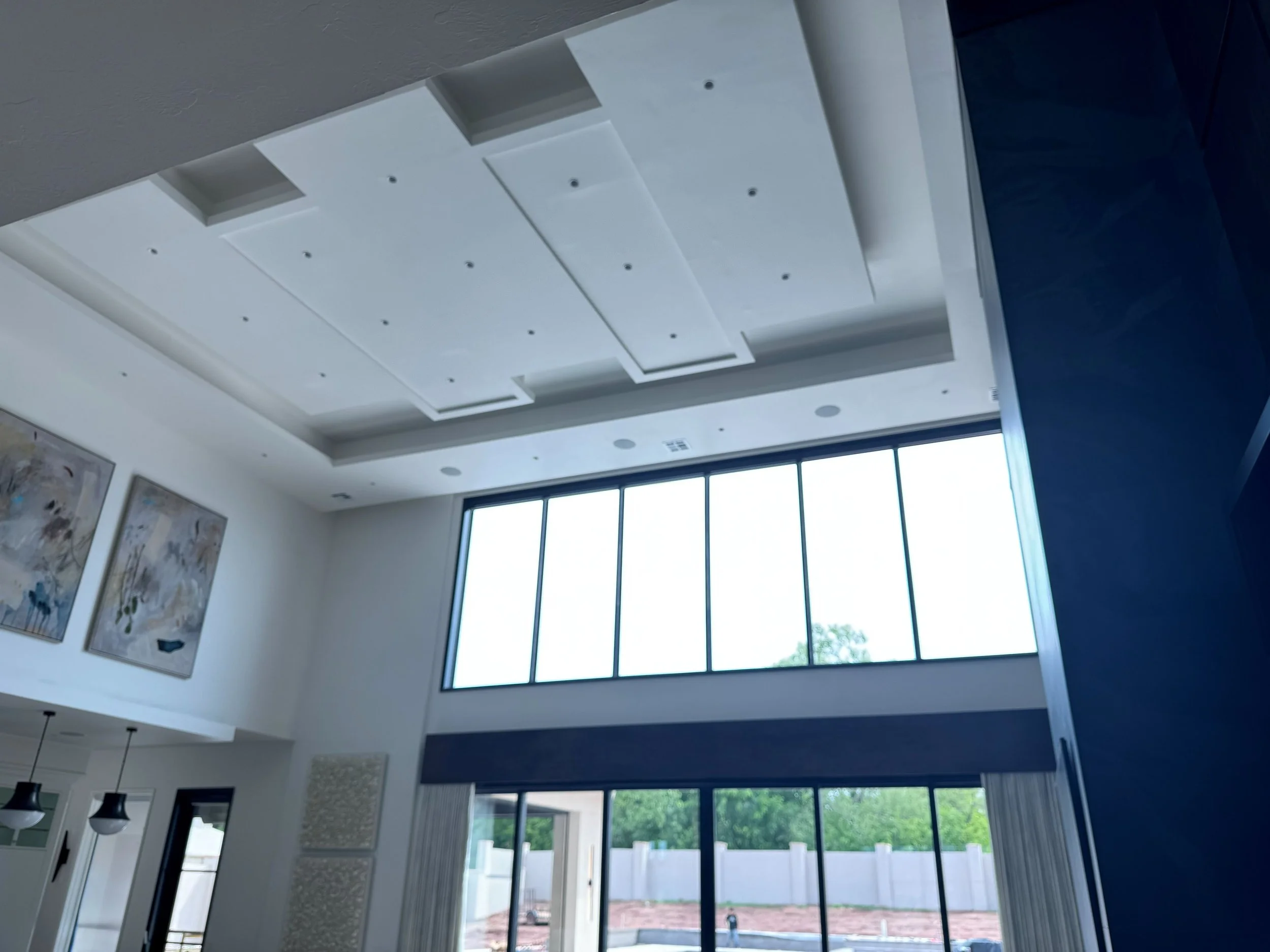 Interior of a modern living room with high ceilings, large windows, and artwork on the walls.