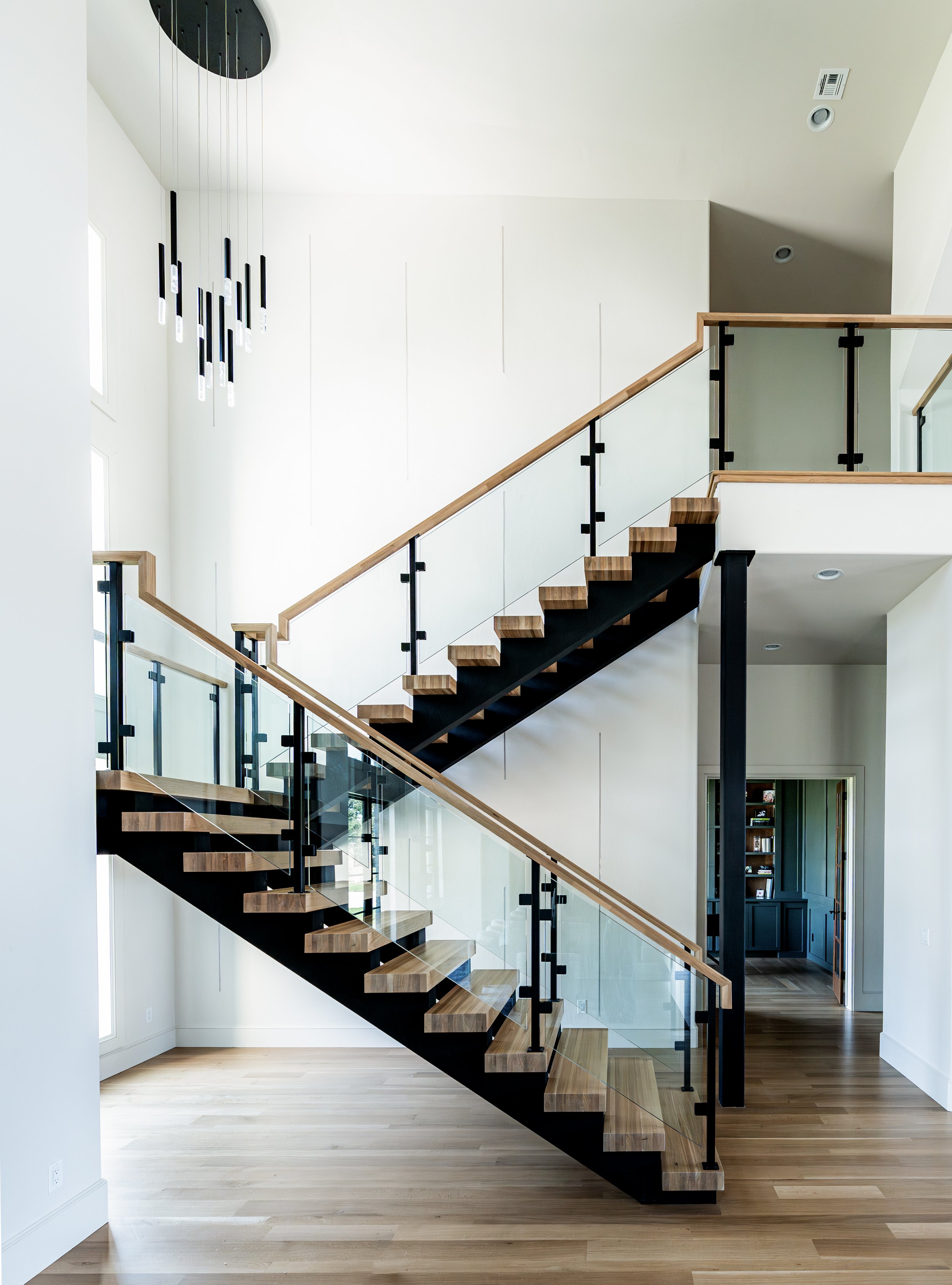 Modern staircase with wooden steps and glass railing in a bright, minimalist home.