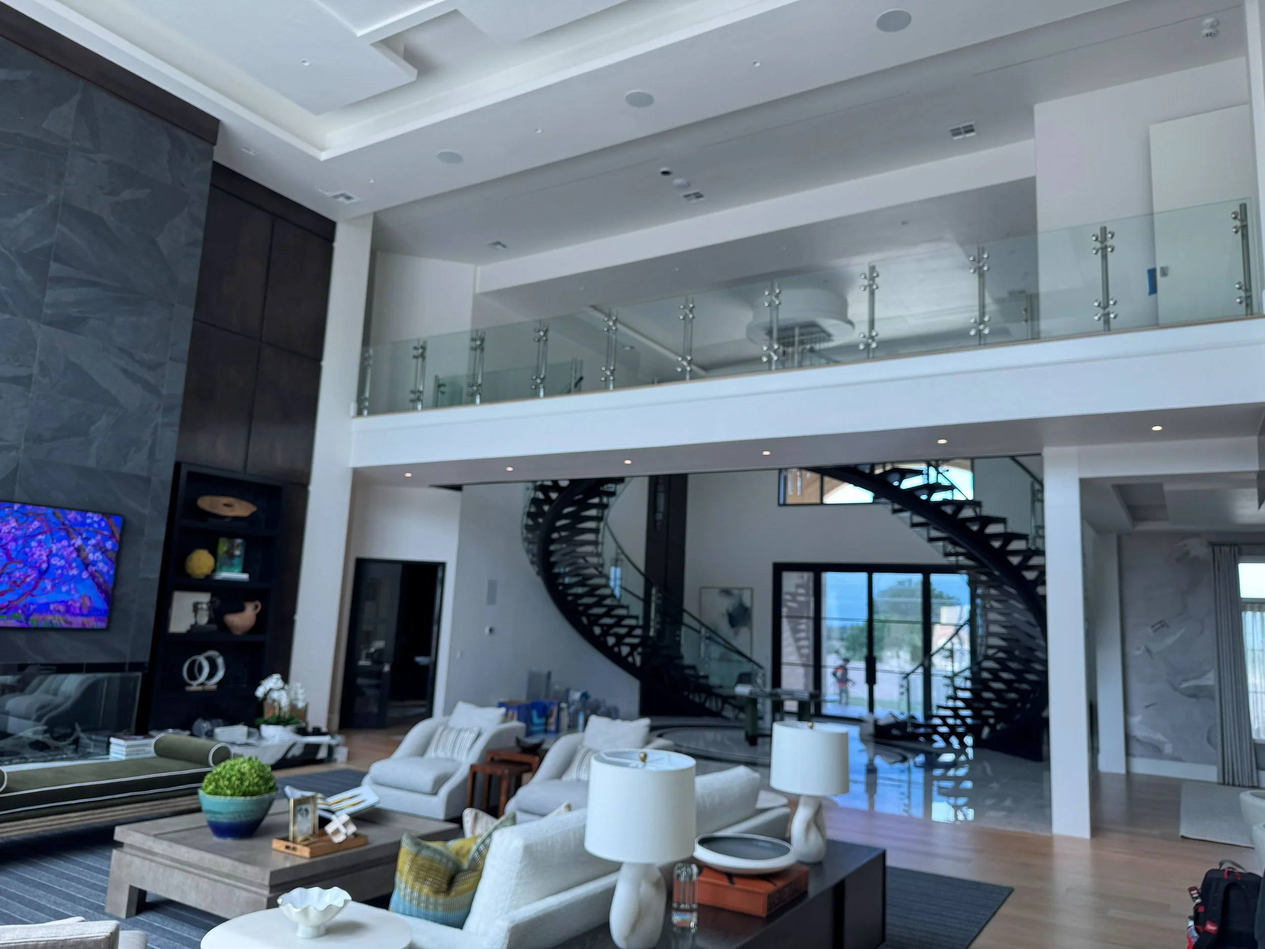 Modern living room with a curved staircase, white furniture, and a glass balcony on the upper floor.